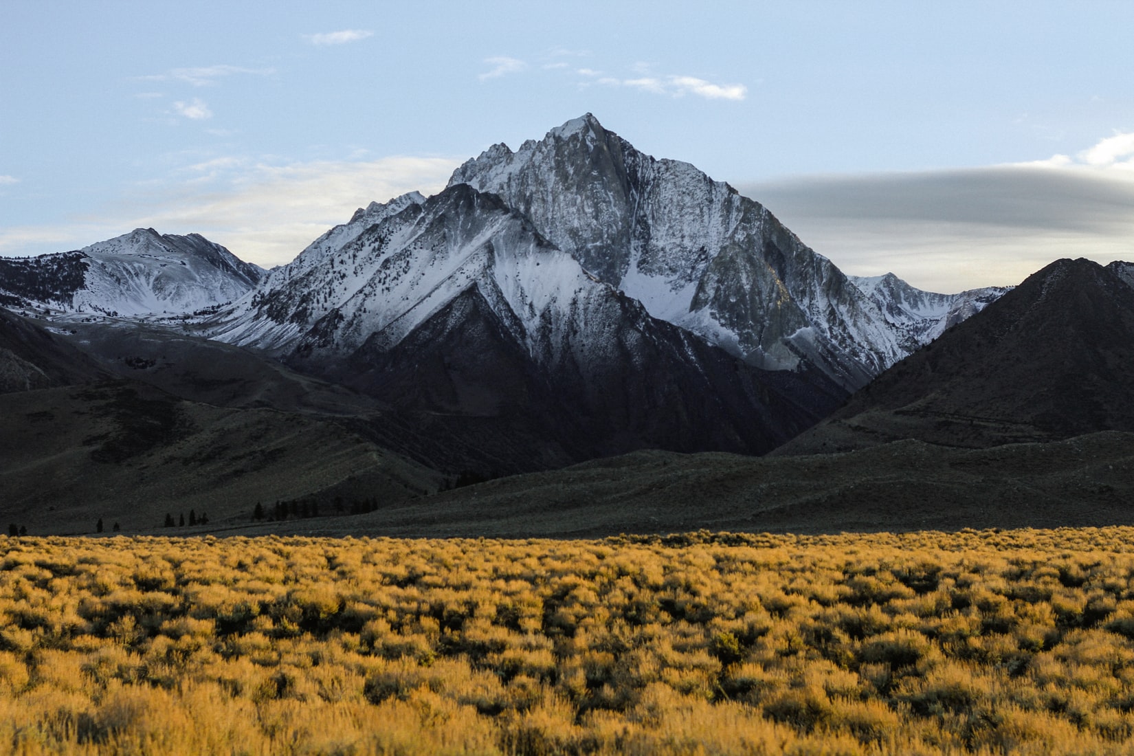 Snow-capped mountain peak rising above a golden valley at sunrise